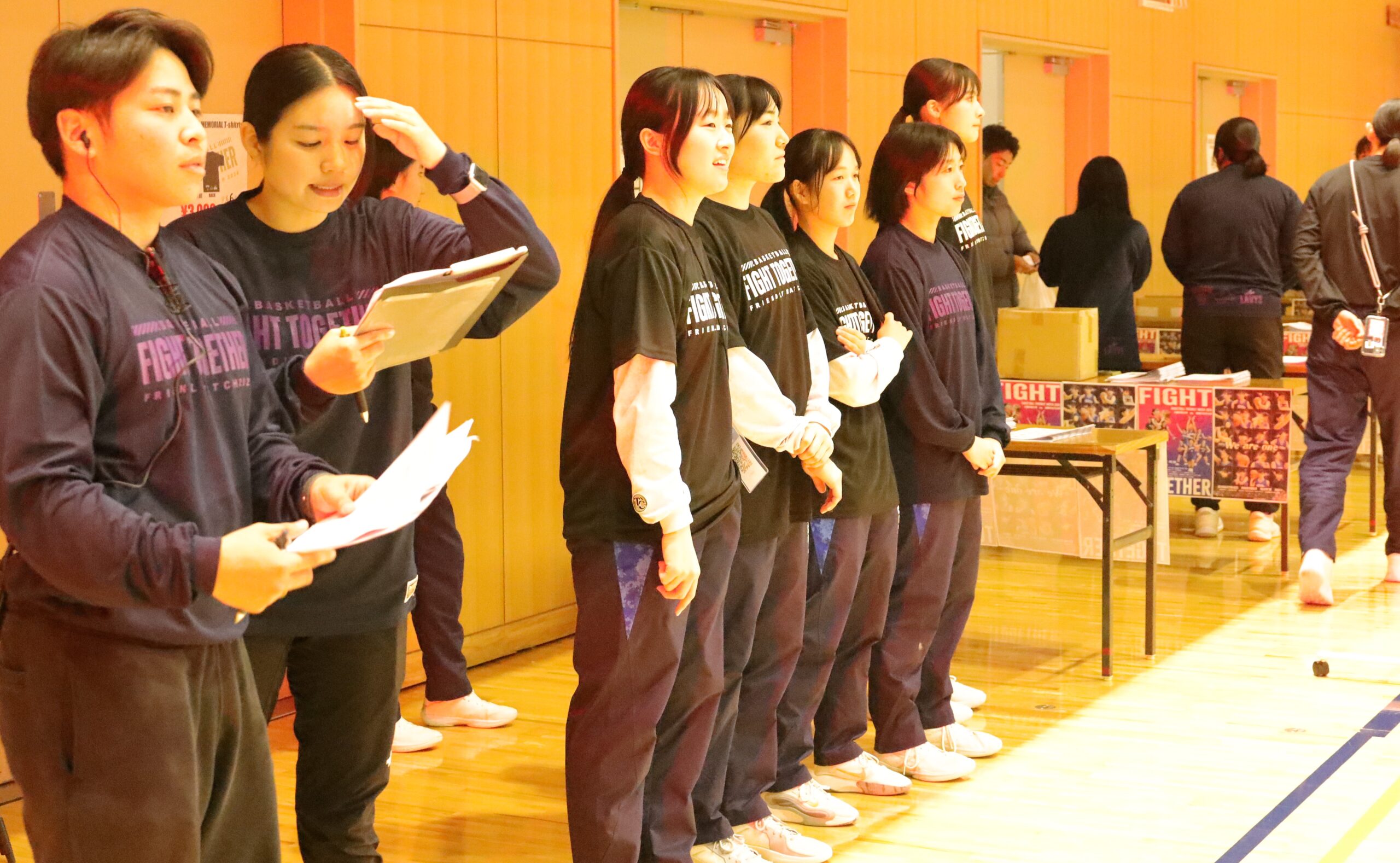 学生スタッフ（ピンクの文字のTシャツ）とバスケットボール部女子の運営スタッフ （白のTシャツ）