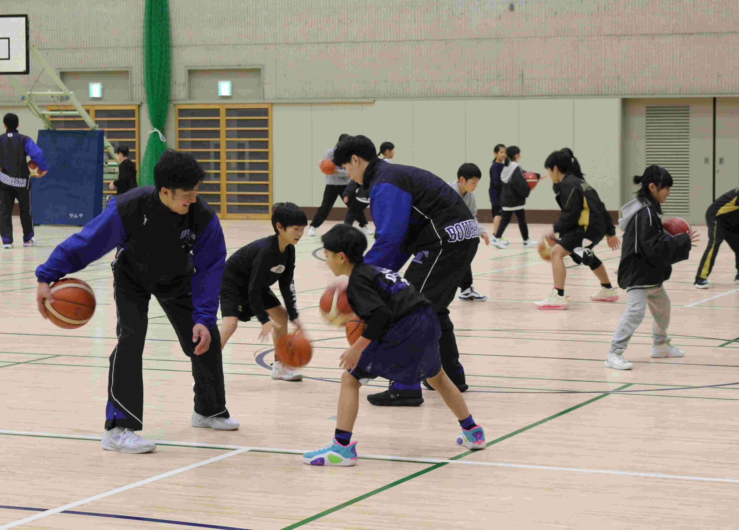 小学生にドリブルを教えるバスケットボール部員。部員も笑顔 【豊岡市提供】