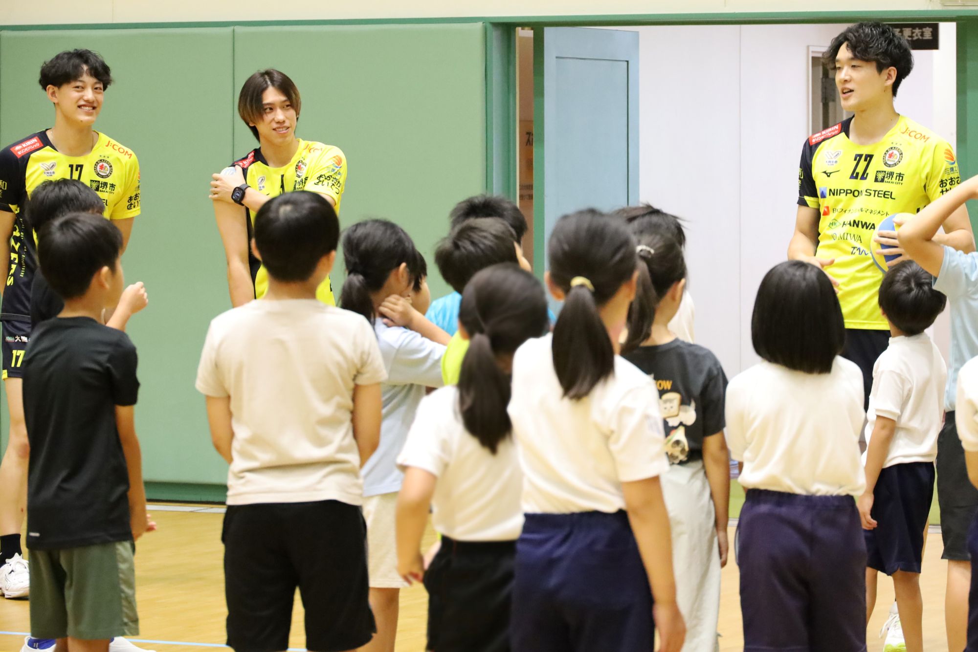 子どもたちにアンダーハンドパスとレシーブの説明をするブレイザーズの選手 向かって右から、柿崎選手、大宅選手、上村選手